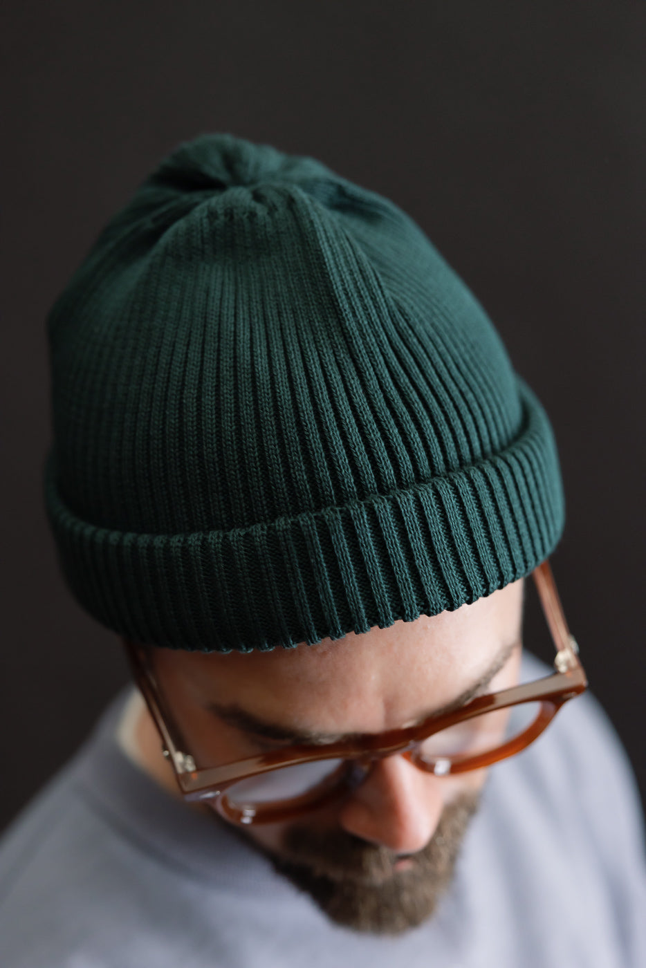 Close-up of front view ribbed cotton roll-up beanie in forest green on male model, 5'9