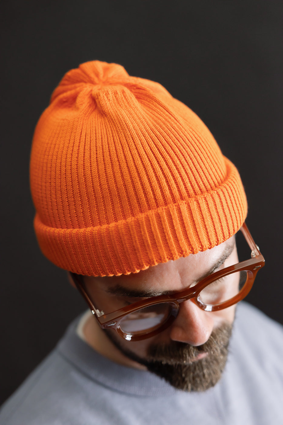 R5021 - Cotton Roll-Up Beanie - Orange showcased on a model's head, featuring a shallow cut with a roll-up hem, highlighting its rib-knit texture and modern, structured look within a premium menswear setting.