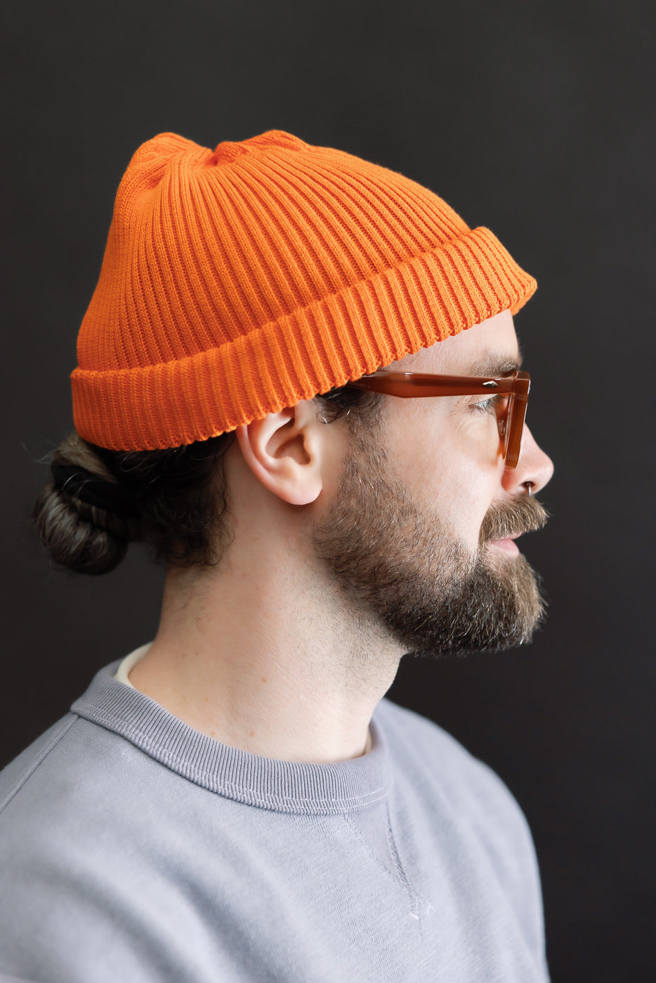 Side-profile of a man wearing the Rototo R5021 - Cotton Roll-Up Beanie in orange, showcasing its shallow-cut design above the ears. The beanie features a 2x2 rib knit and roll-up hem.