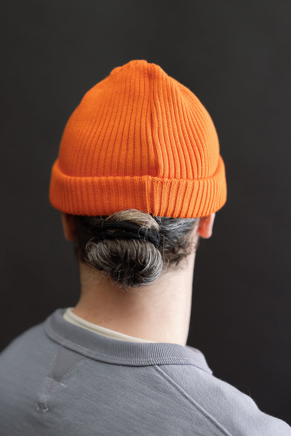 Back view of a person wearing the R5021 - Cotton Roll-Up Beanie - Orange, showcasing its shallow cut and ribbed texture, styled with a gray sweatshirt, highlighting the beanie's unique fit and design.