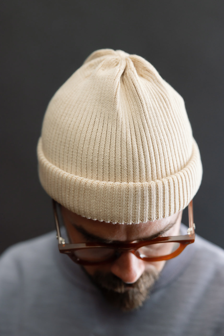 Close-up of raw beige cotton roll-up beanie on male model, front top view, rib knit texture