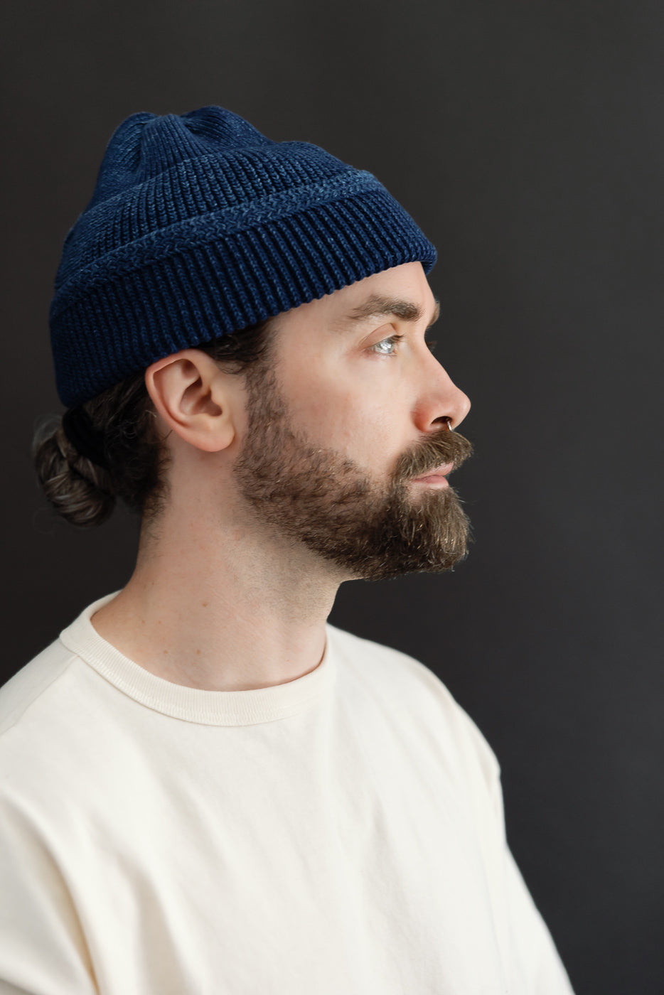 Close-up side profile of a male model wearing a navy blue ribbed knit beanie.