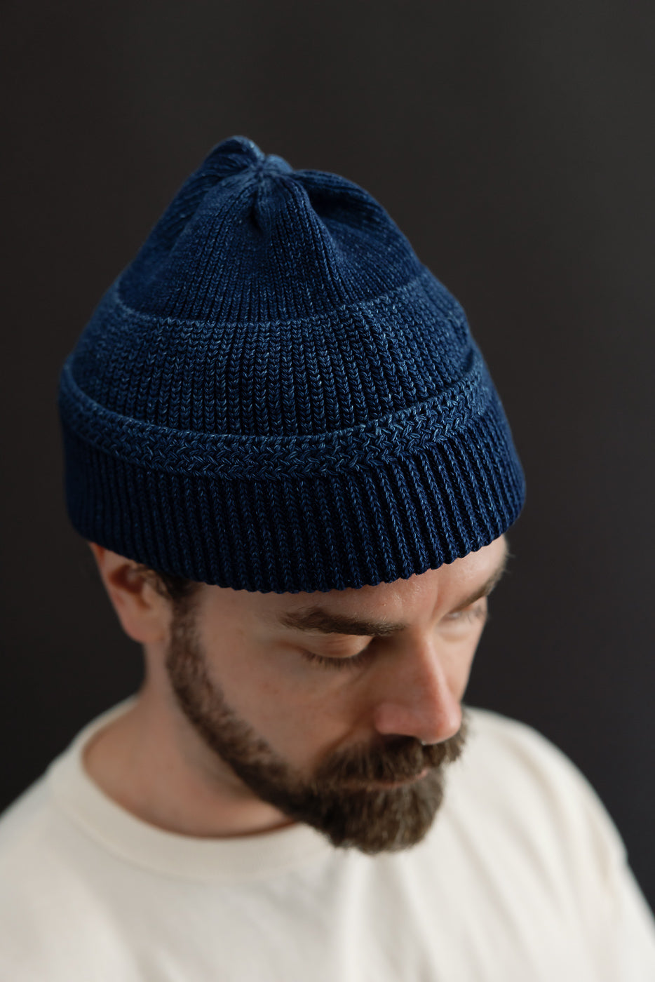 Close-up front view of a male model wearing a navy blue ribbed knit beanie hat.