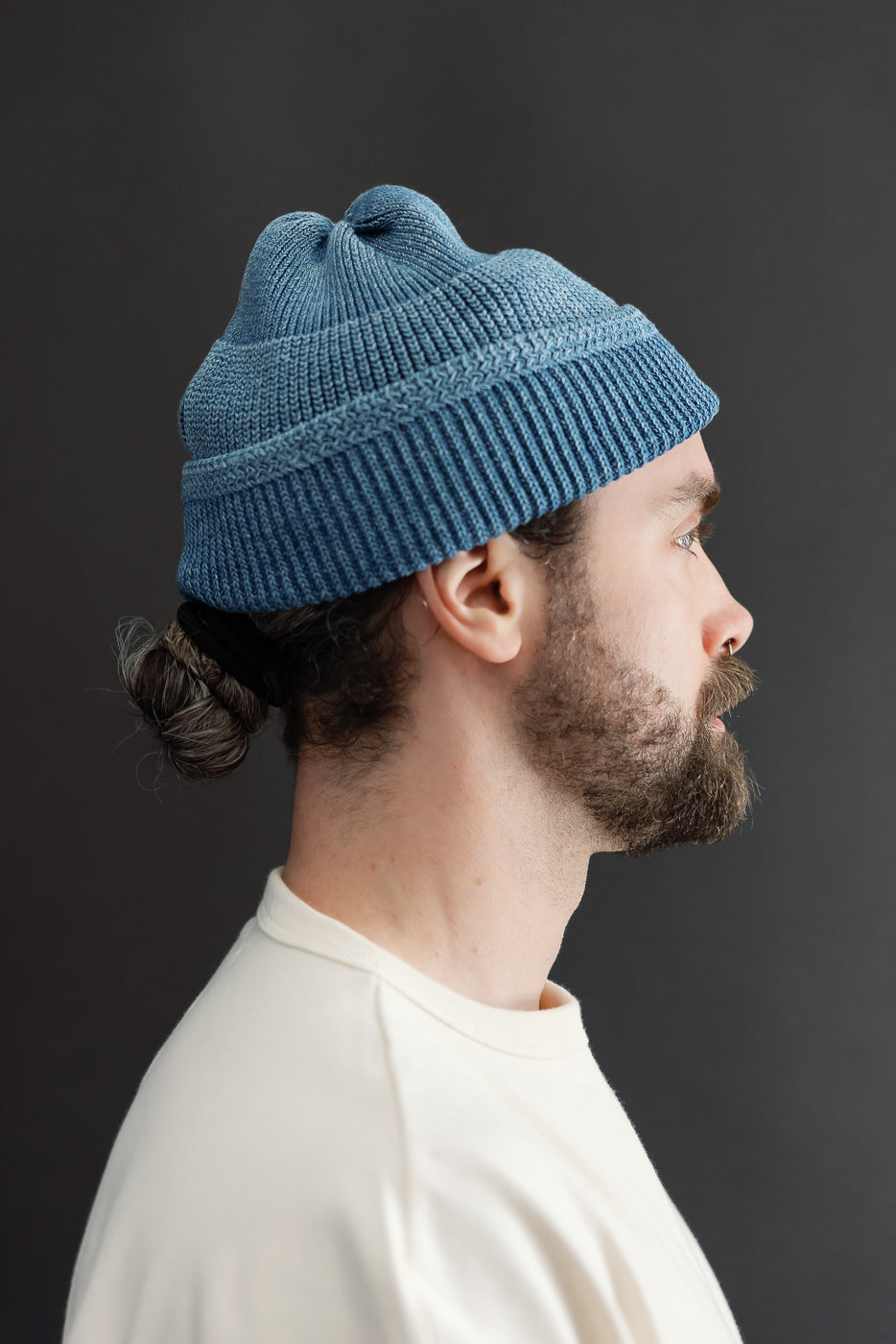 Side profile close-up of a male model wearing a blue ribbed knit beanie.