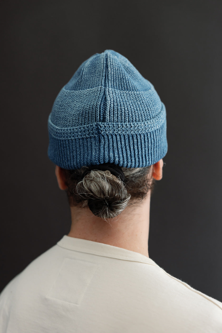 Back view close-up of a male model wearing a blue ribbed knit beanie.