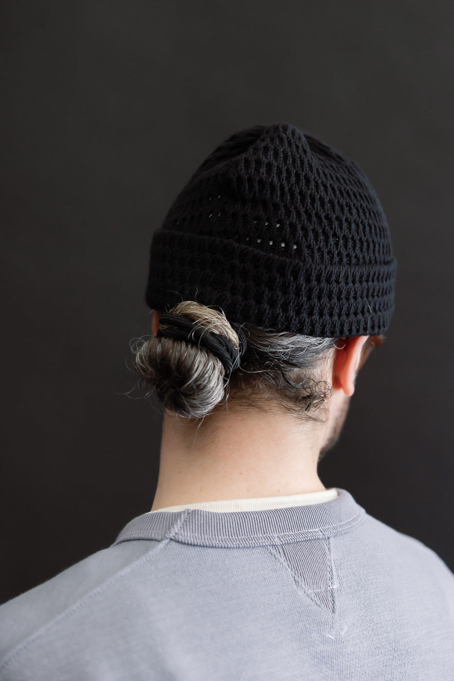 Back view close-up of recycled cotton open knit beanie in light black on male model, 5'9