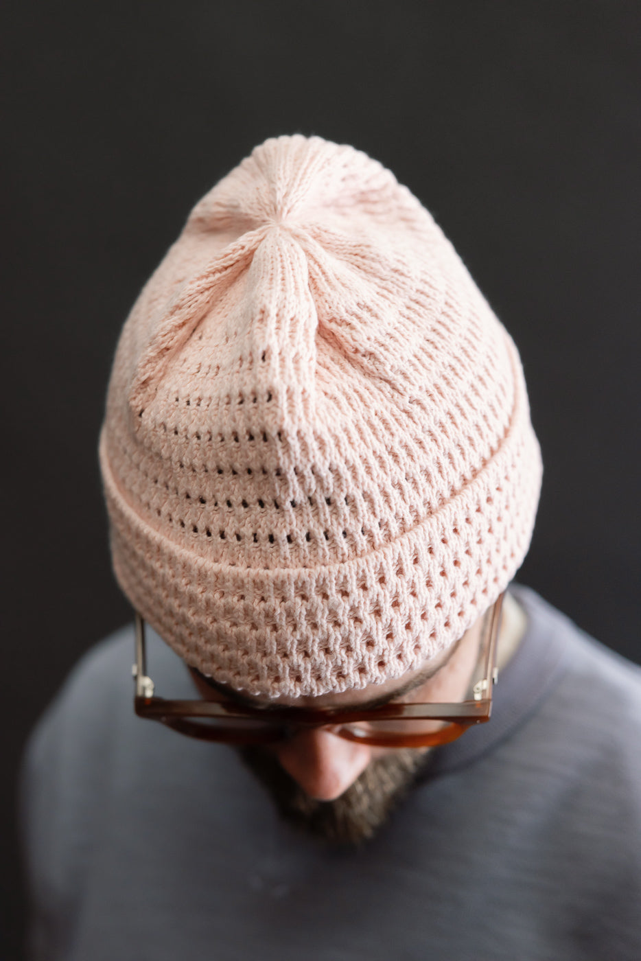 Close-up top view of a light pink recycled cotton open knit beanie on a male model, 5'9