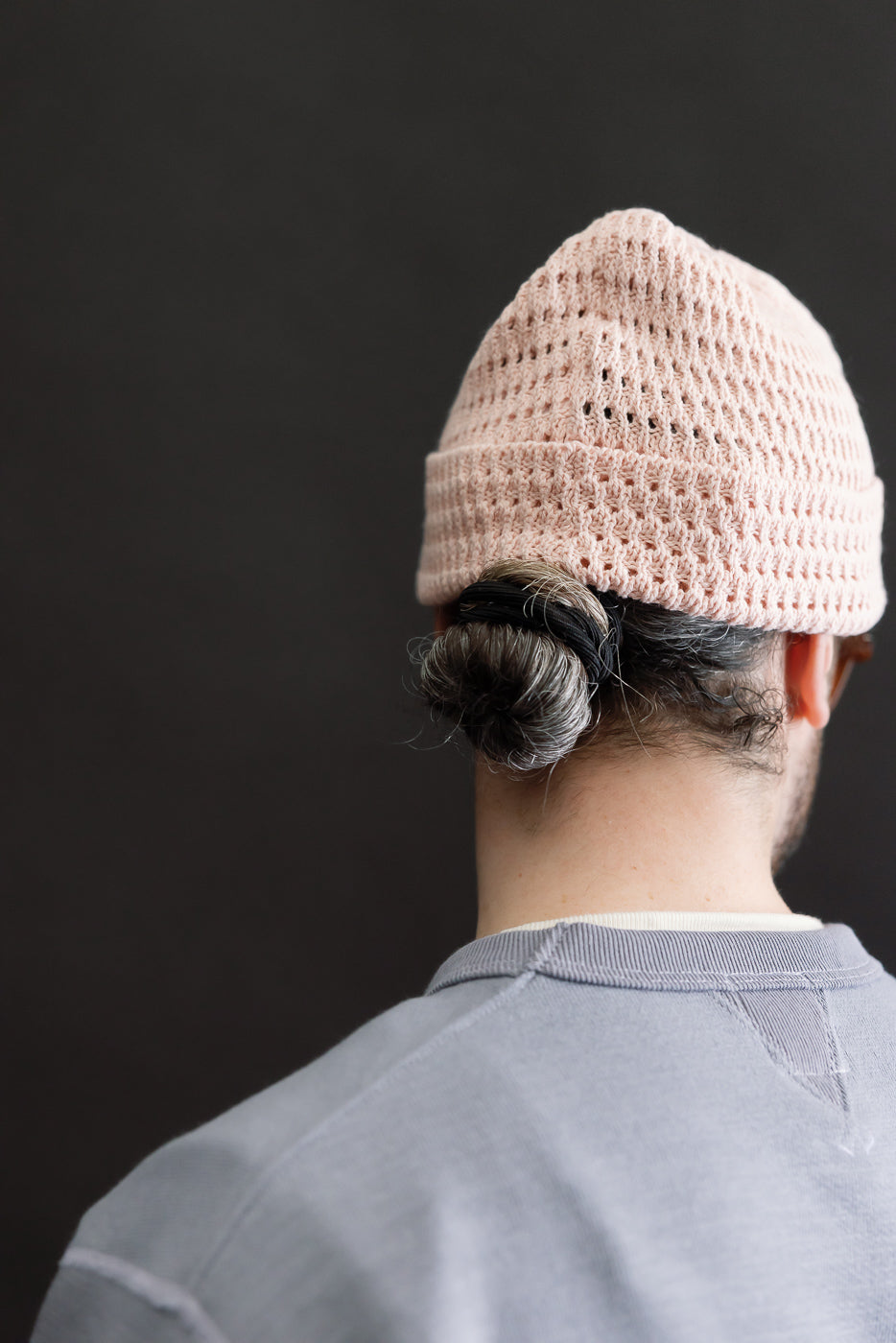 Back view close-up of a light pink recycled cotton open knit beanie on male model, showing knit texture detail. Model is 5'9