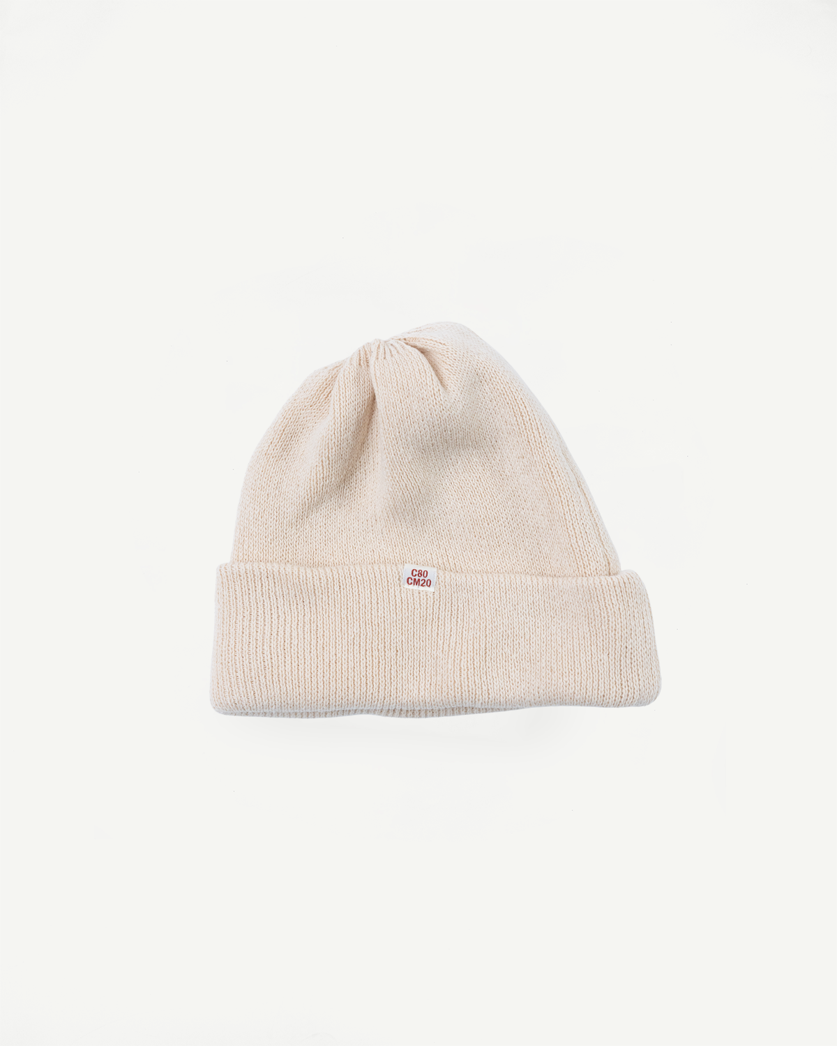 Front view flat lay of a cream ribbed knit beanie with a small red brand tag on the cuff.