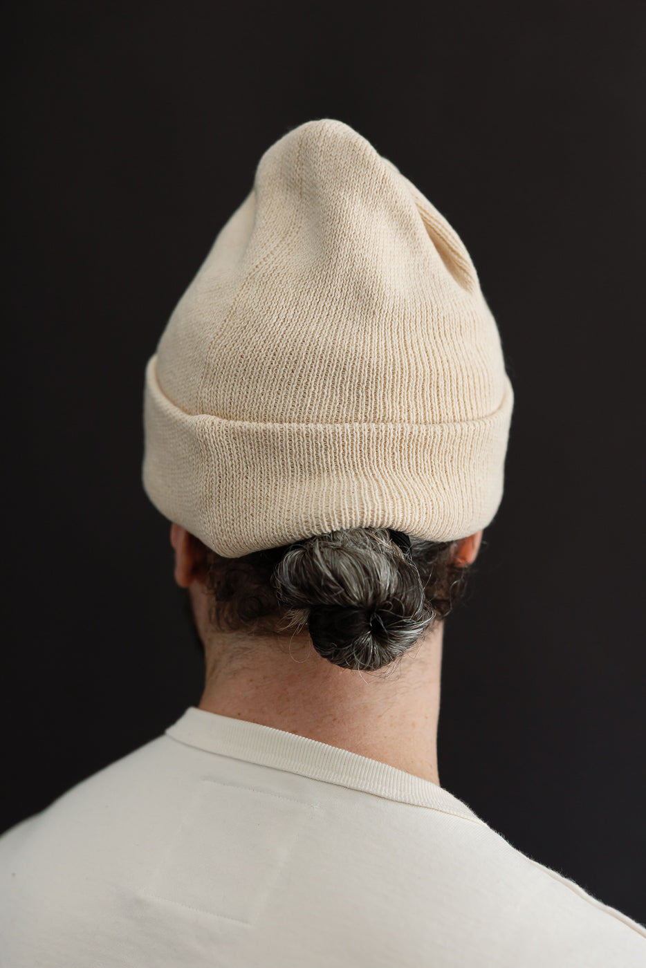 Back view close-up of a male model wearing a cream knit beanie and white t-shirt.