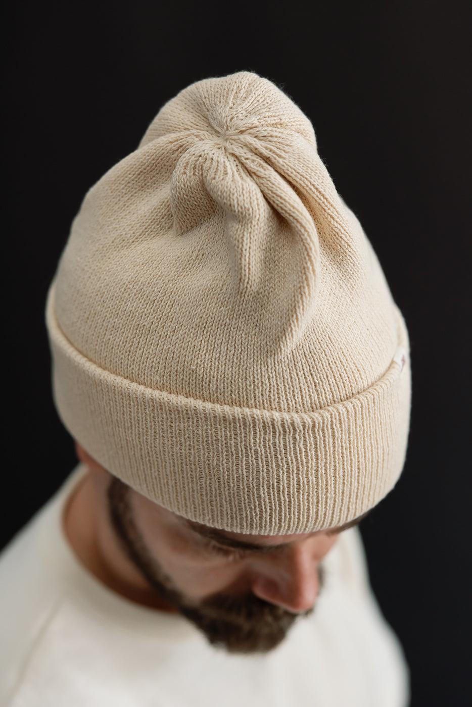 Close-up front view of a beige ribbed knit beanie on a male model.