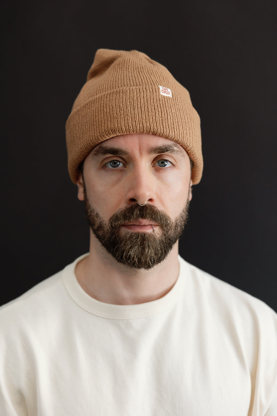 Close-up front view of a male model wearing a tan ribbed beanie hat.