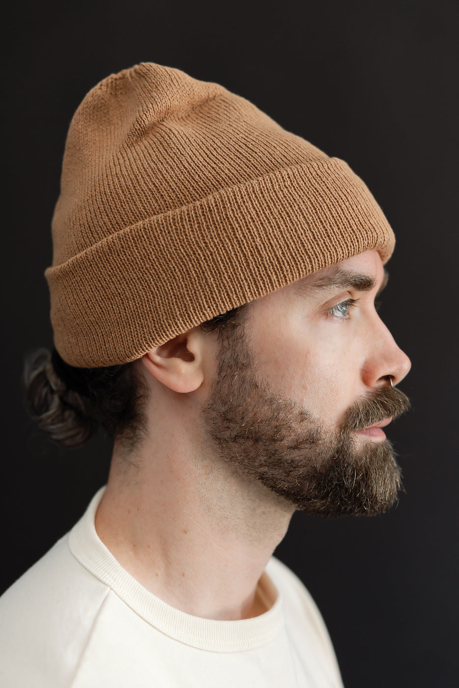 Close-up side profile of a male model wearing a tan ribbed knit beanie.