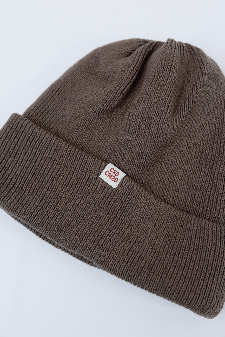 Close-up of the front of a brown ribbed knit beanie showing the fabric texture and C80 CM20 tag.