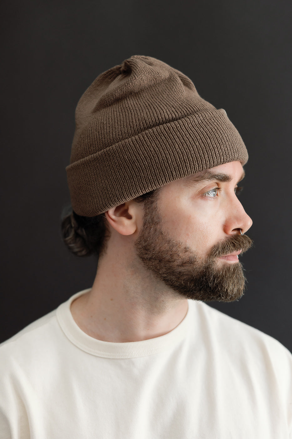 Close-up profile view of a male model wearing a brown ribbed knit beanie hat.
