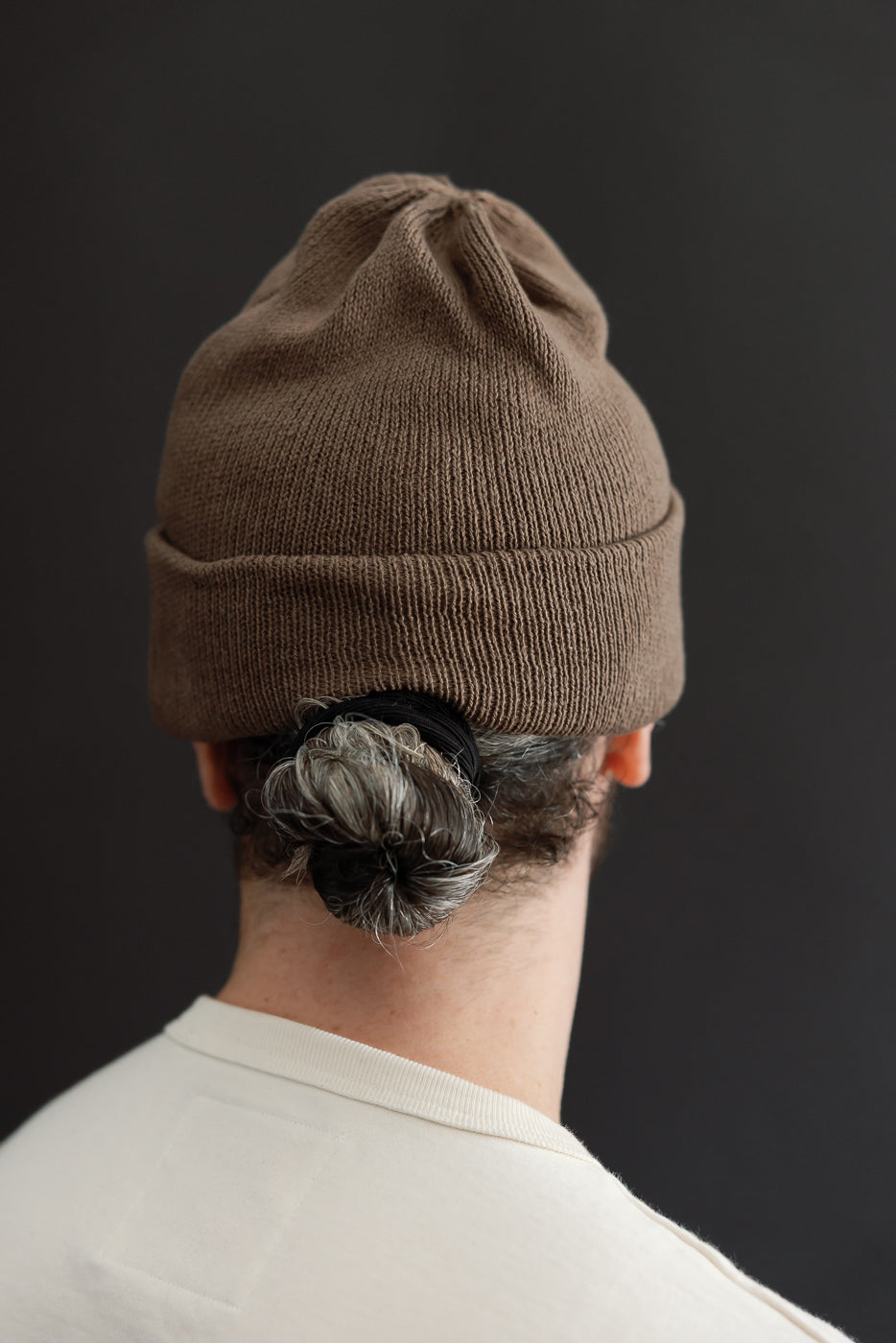 Back view close-up of a brown ribbed knit beanie worn by a male model, 5'9