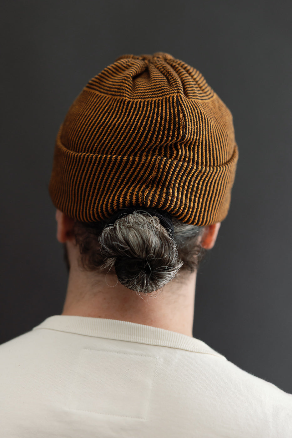 Back view close-up of a male model wearing a brown ribbed beanie and white t-shirt.