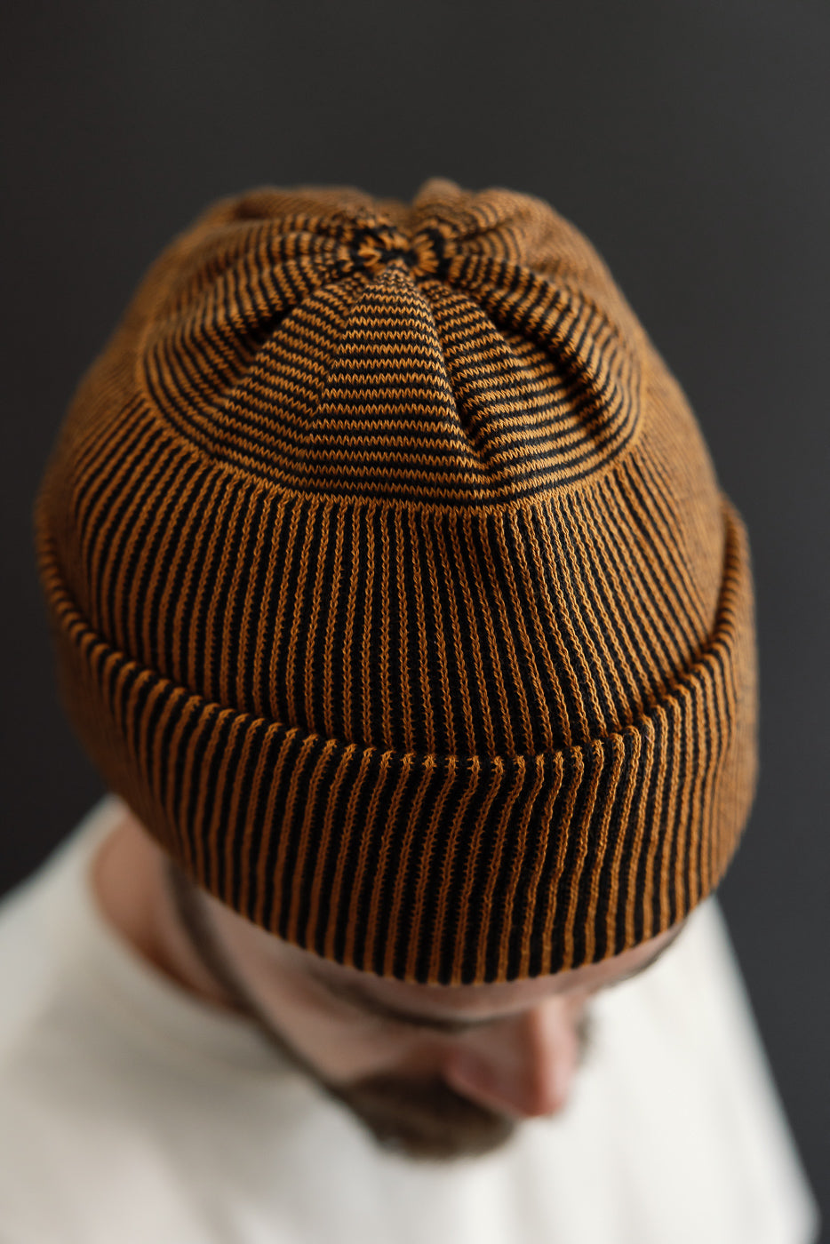 Close-up top view of a brown and black striped knit beanie worn by a male model.