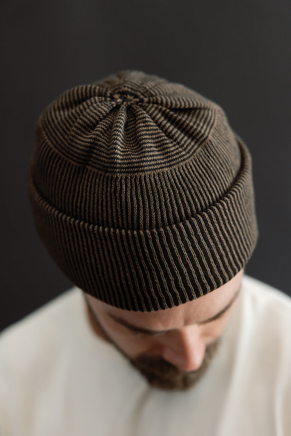Close-up front view of a male model wearing a brown ribbed knit beanie hat.