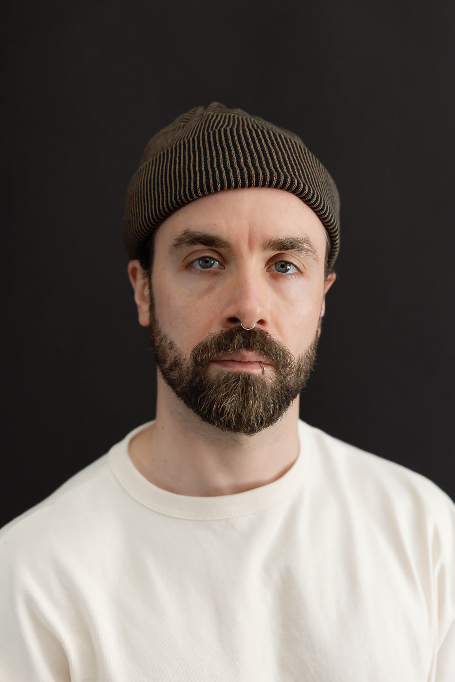 Close-up front view of a male model with an athletic build wearing a brown ribbed beanie and white t-shirt.