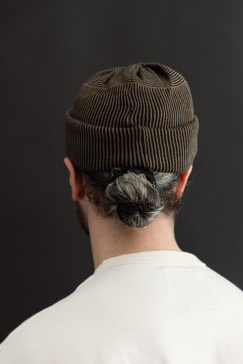 Back view close-up of a male model wearing a brown ribbed beanie and white t-shirt.