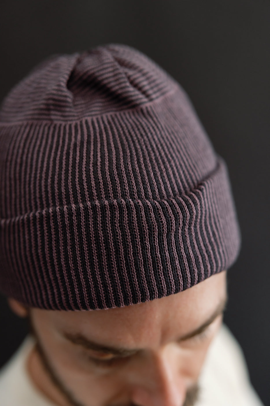 Close-up front view of a male model wearing a dark purple ribbed knit beanie.