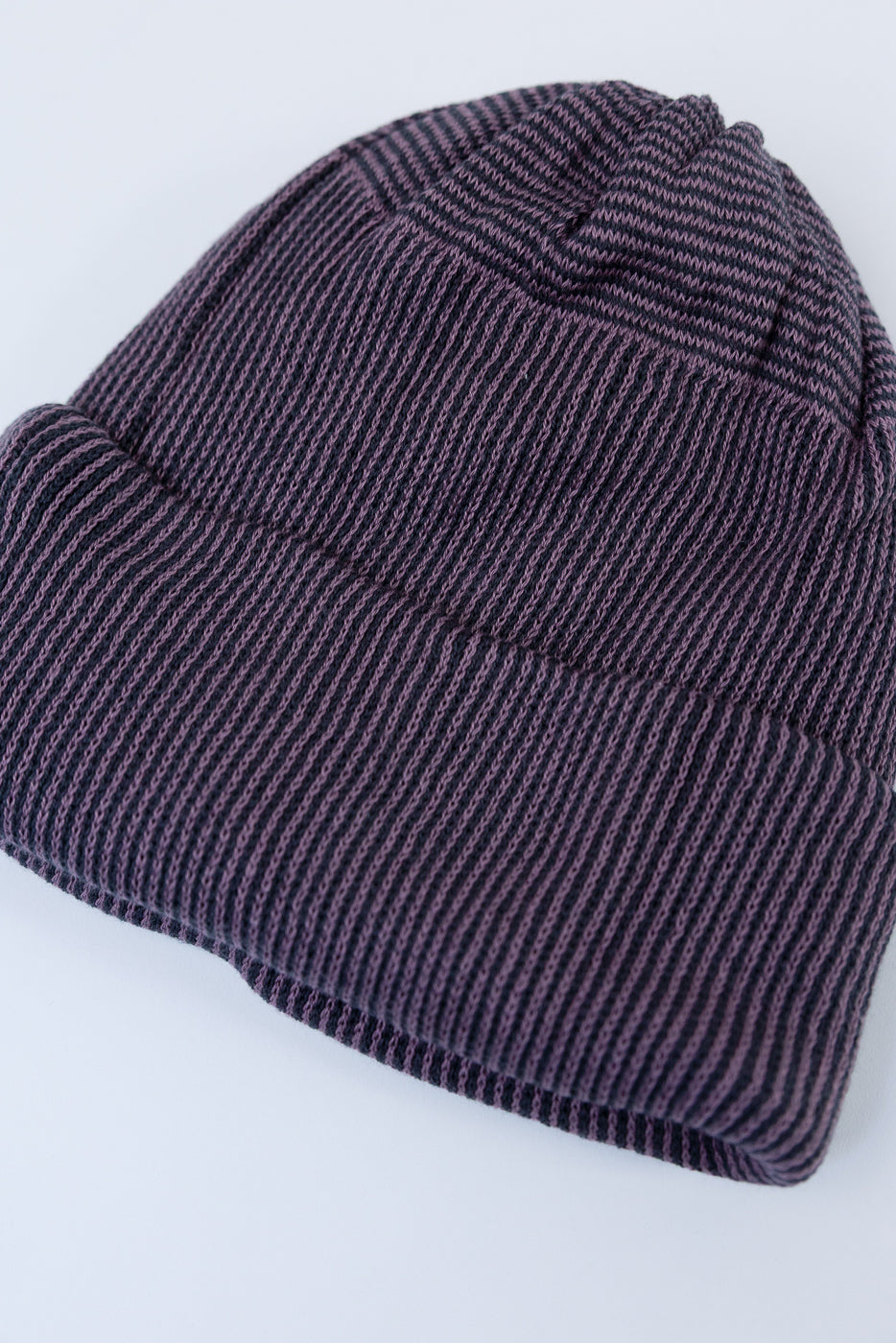 Close-up flat lay of the front of a purple ribbed knit beanie showing fabric texture.