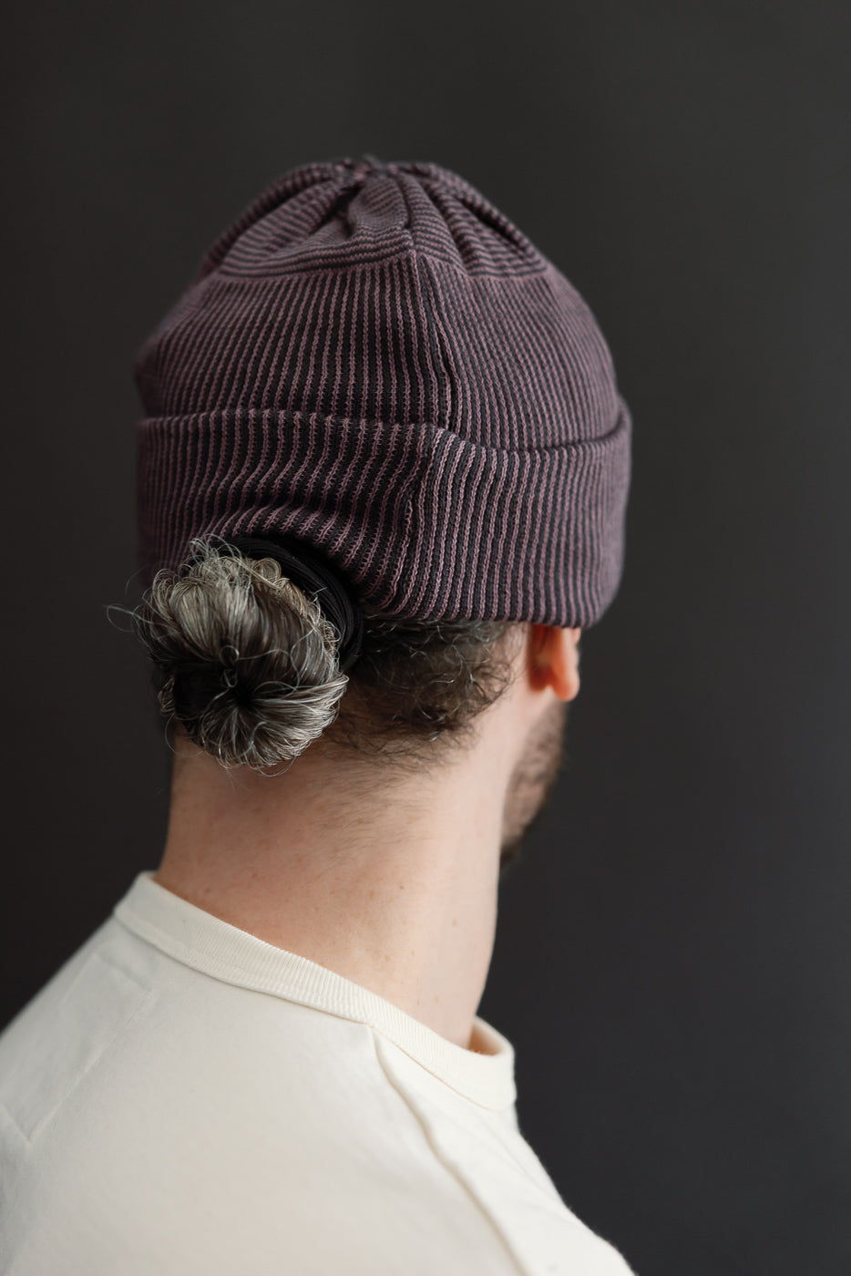 Close-up back view of a male model wearing a ribbed purple beanie hat.
