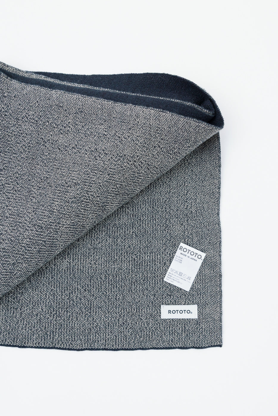 Flat lay close-up of the front of a grey textured knit scarf with a white Rototo brand tag.