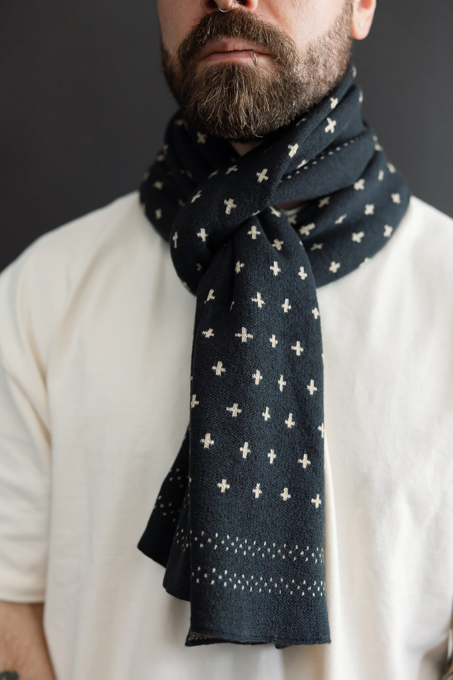Close-up, front view of a male model wearing a black patterned scarf with white cross motifs.