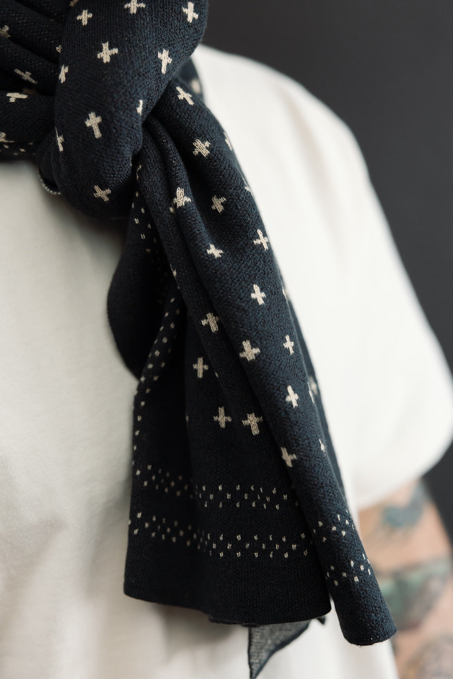 Close-up of the front of a black knit scarf with white cross patterns worn over a white t-shirt.