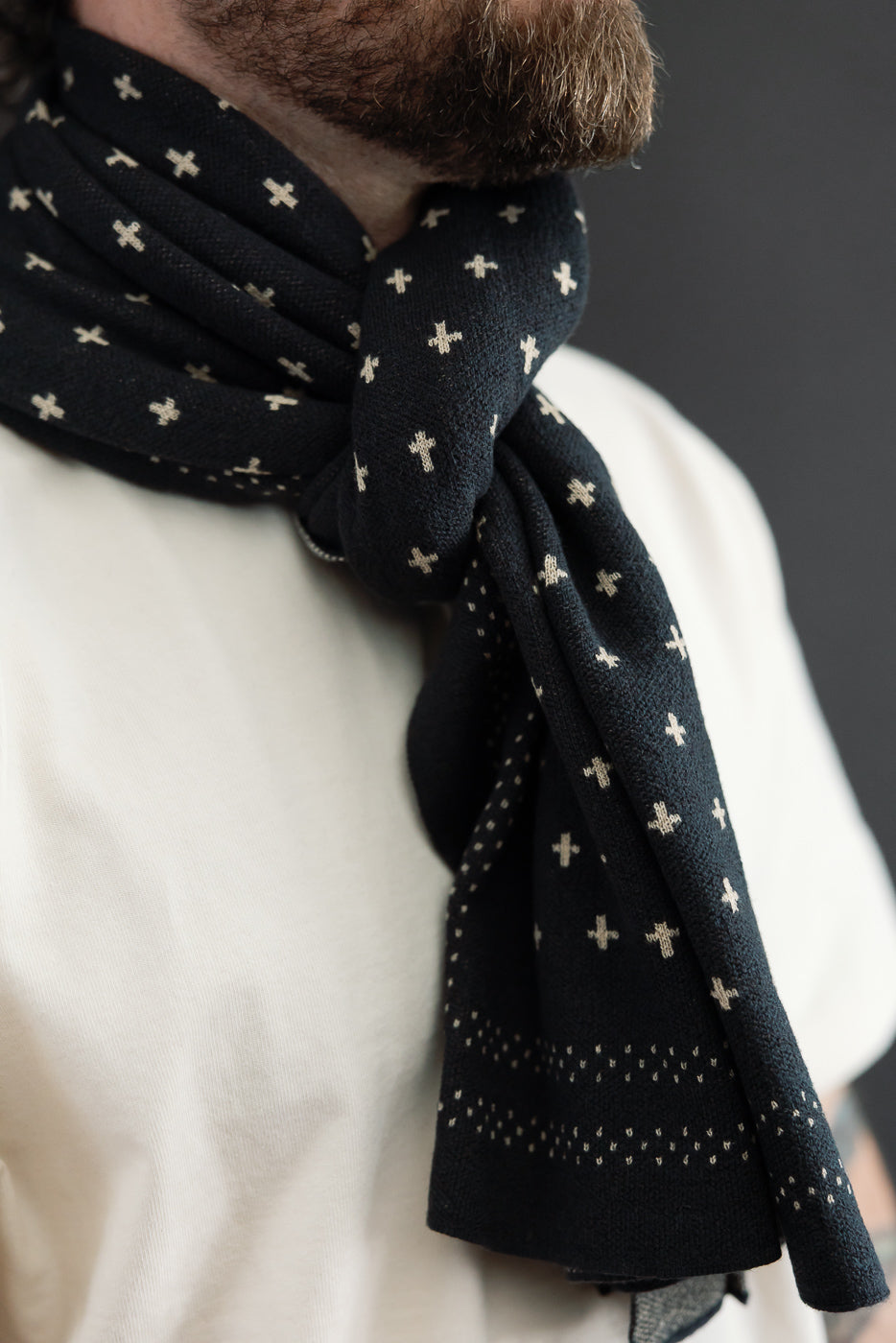 Close-up, front view of a male model wearing a black knit scarf with white cross patterns.