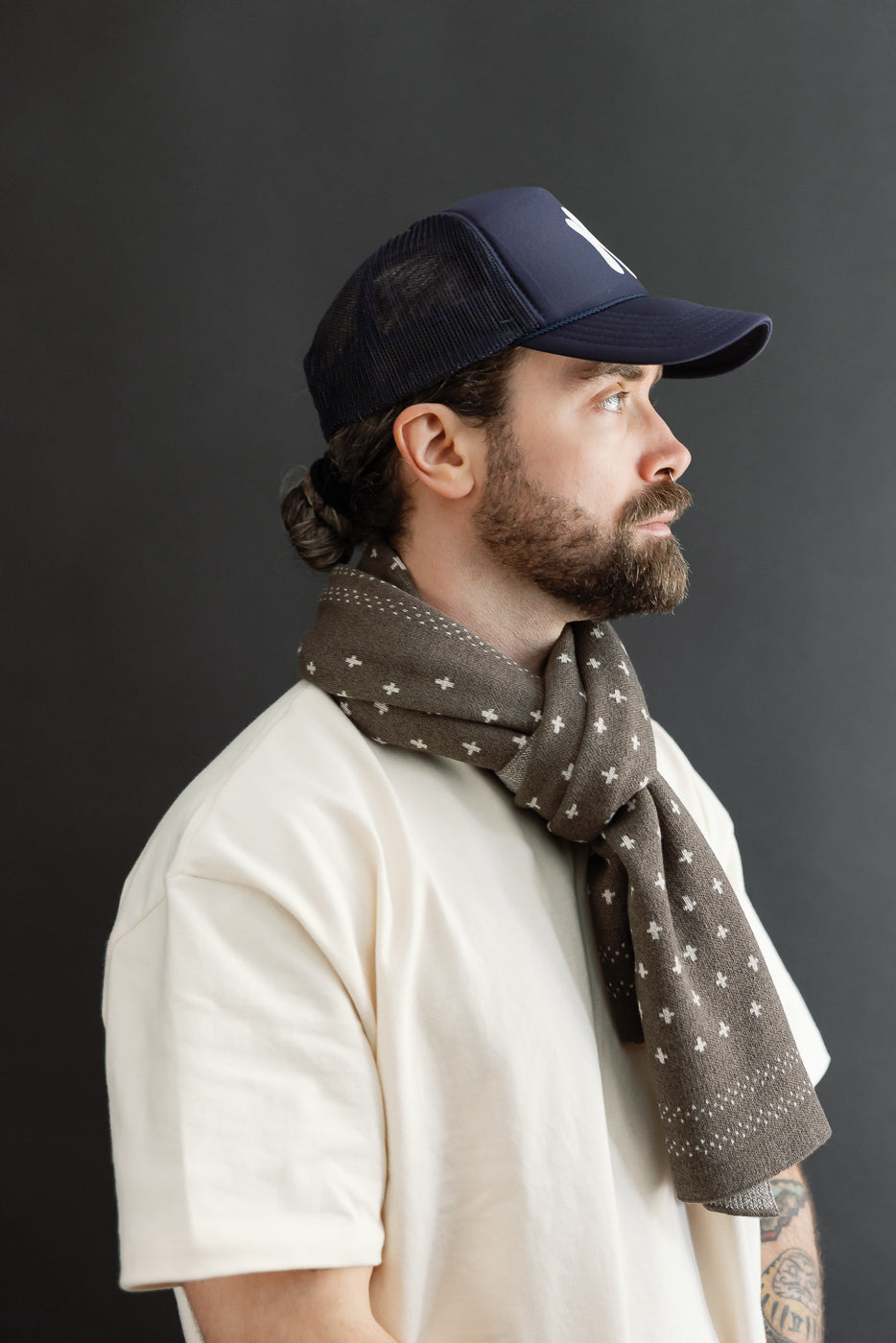 Side profile, close-up of a male model with an athletic build wearing a navy cap and patterned scarf.