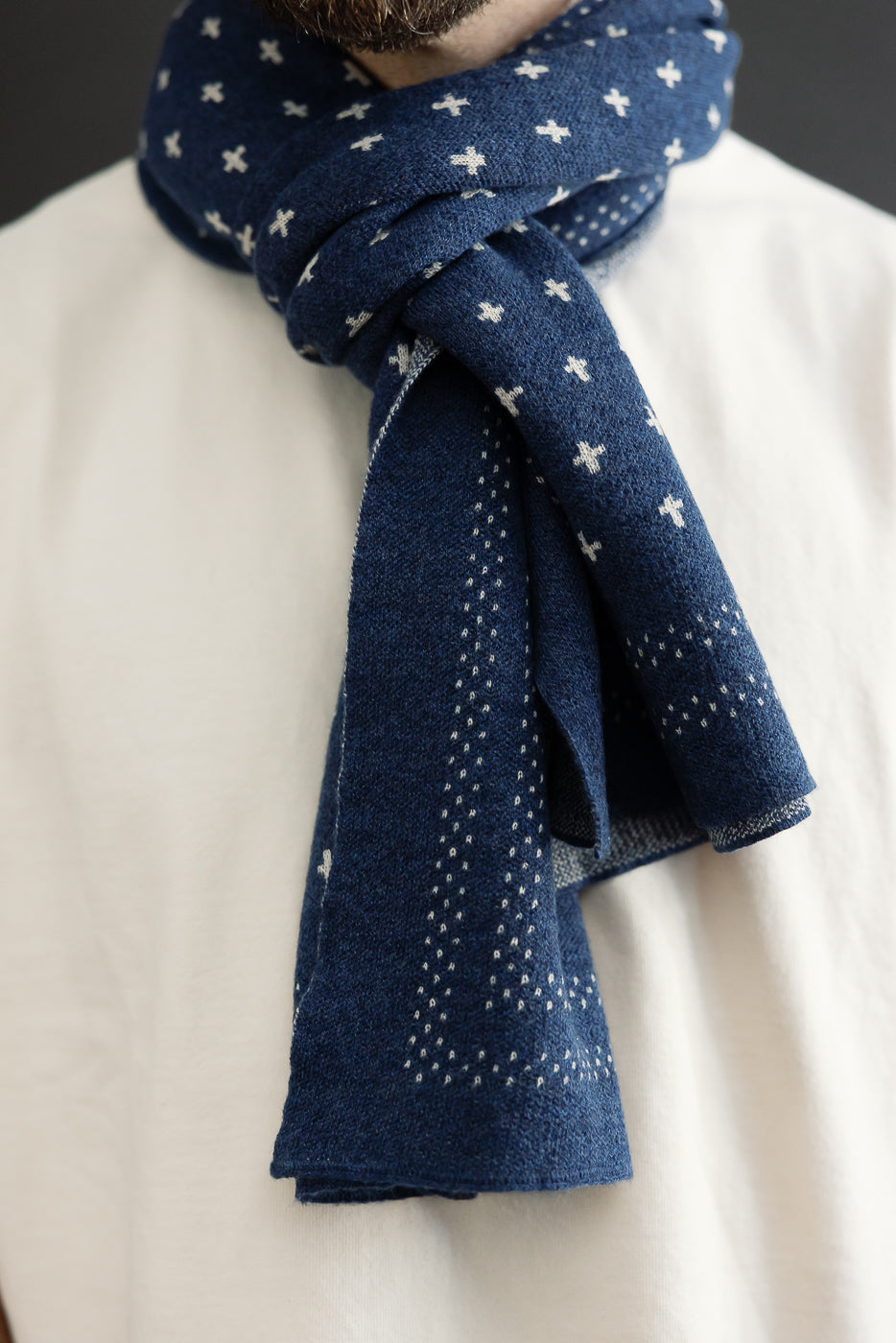 Close-up front view of a male model wearing a navy blue patterned cotton scarf tied around his neck.