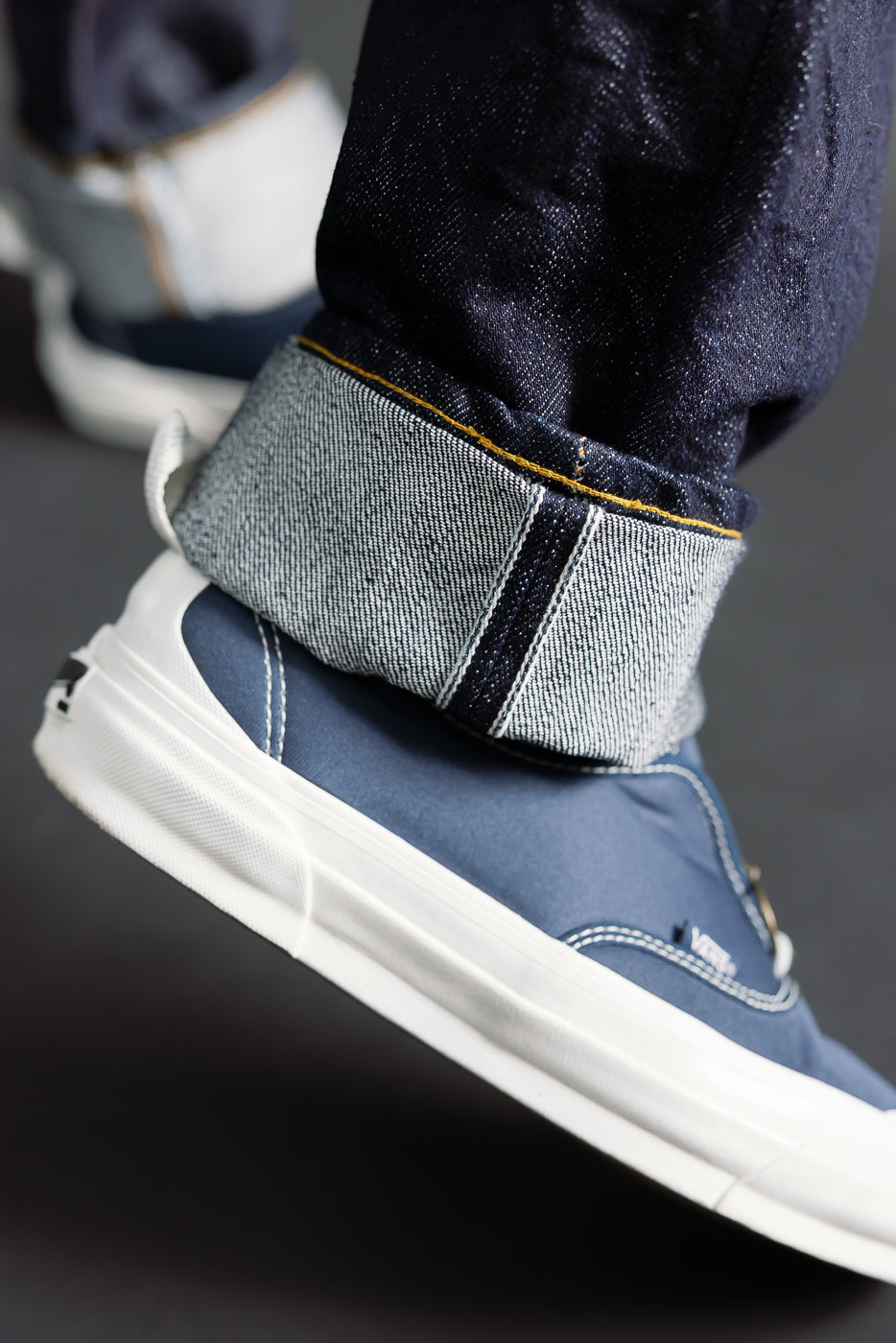 Close-up of male model's cuffed Samurai S0710xx 15oz limited washi selvedge denim showing side seam and fabric texture above sneaker, Dant casual apparel.