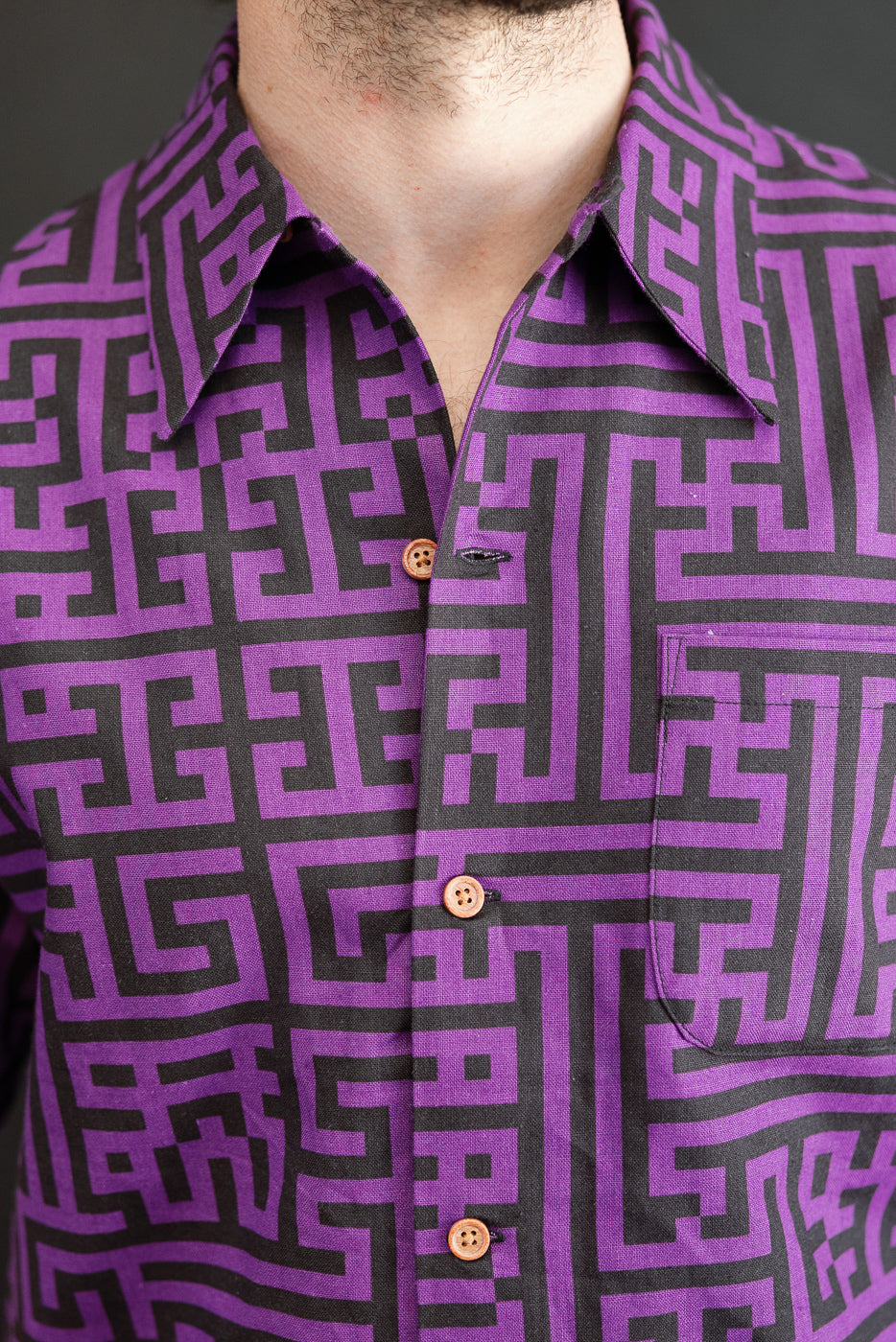 Close-up front view of male model wearing purple & black geometric print shirt with button-down collar and chest pocket