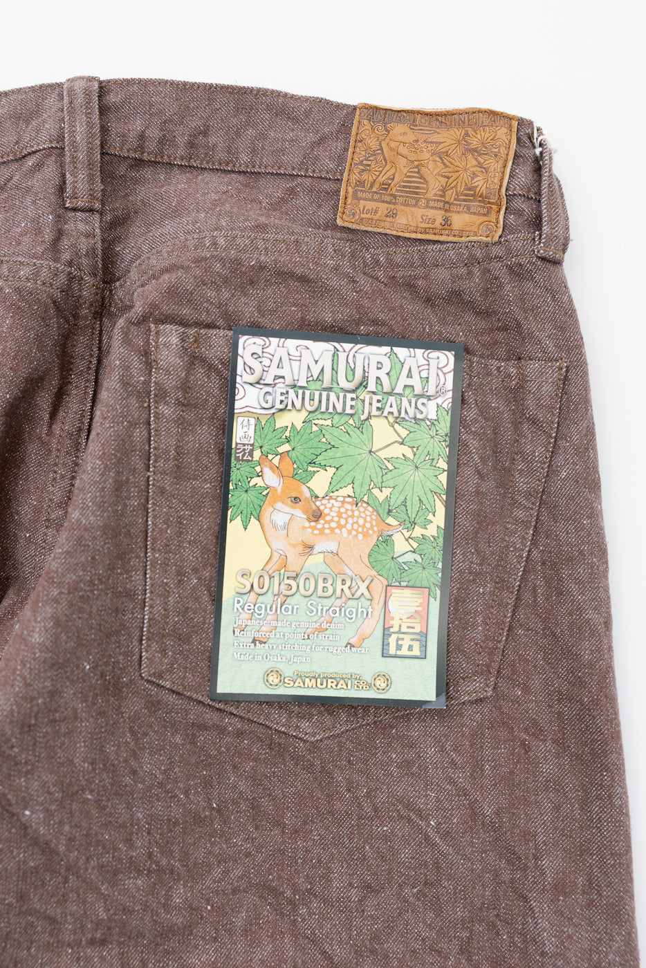 Back view close-up of brown Samurai selvedge jeans, showing leather patch and product tag on rear pocket