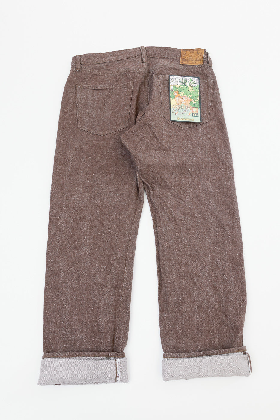 Back view flat lay of brown selvedge jeans with cuffed hems, leather patch, and Samurai patch on right pocket