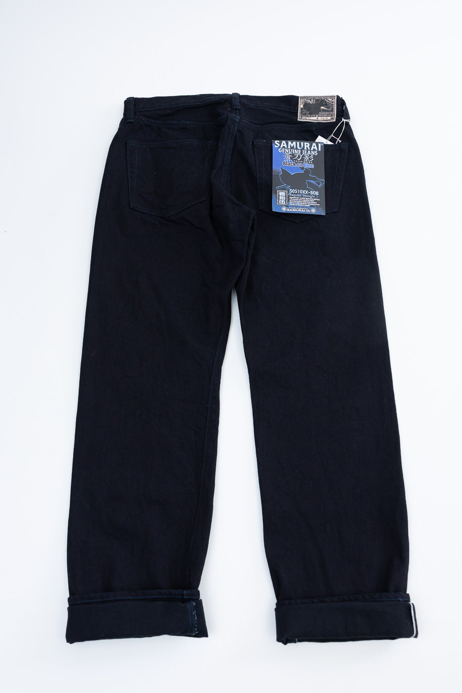 Flat lay of Samurai S0510XX Aoki Tachikage black blue selvedge denim jeans, back view, showing rear pockets, tags, and signature straight leg hem.