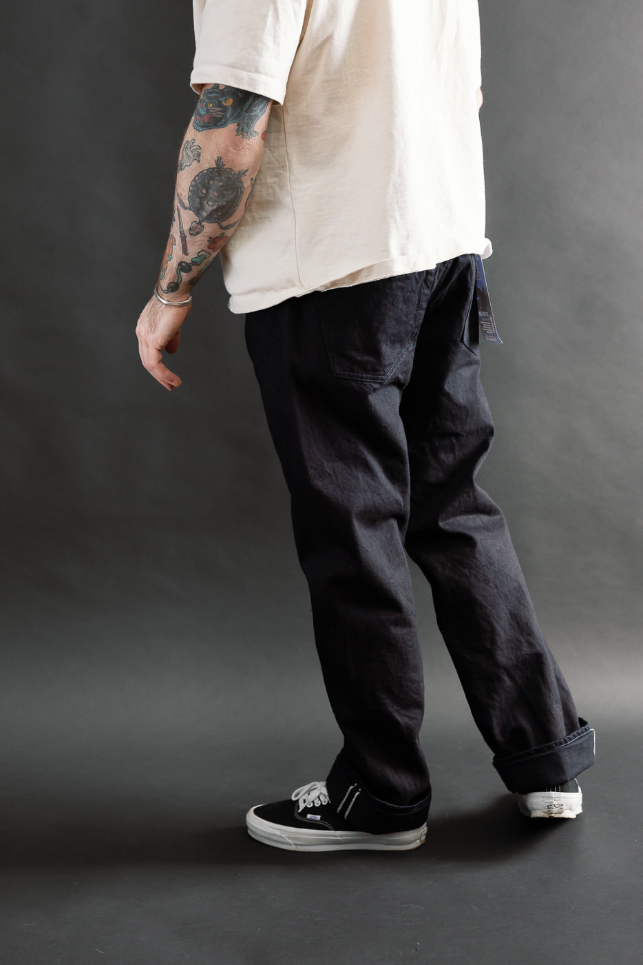 Male model 5'9 165lbs athletic build wearing Samurai S0510XX Aoki Tachikage black blue selvedge denim, regular straight fit, rear side view, casual setting at Dant.