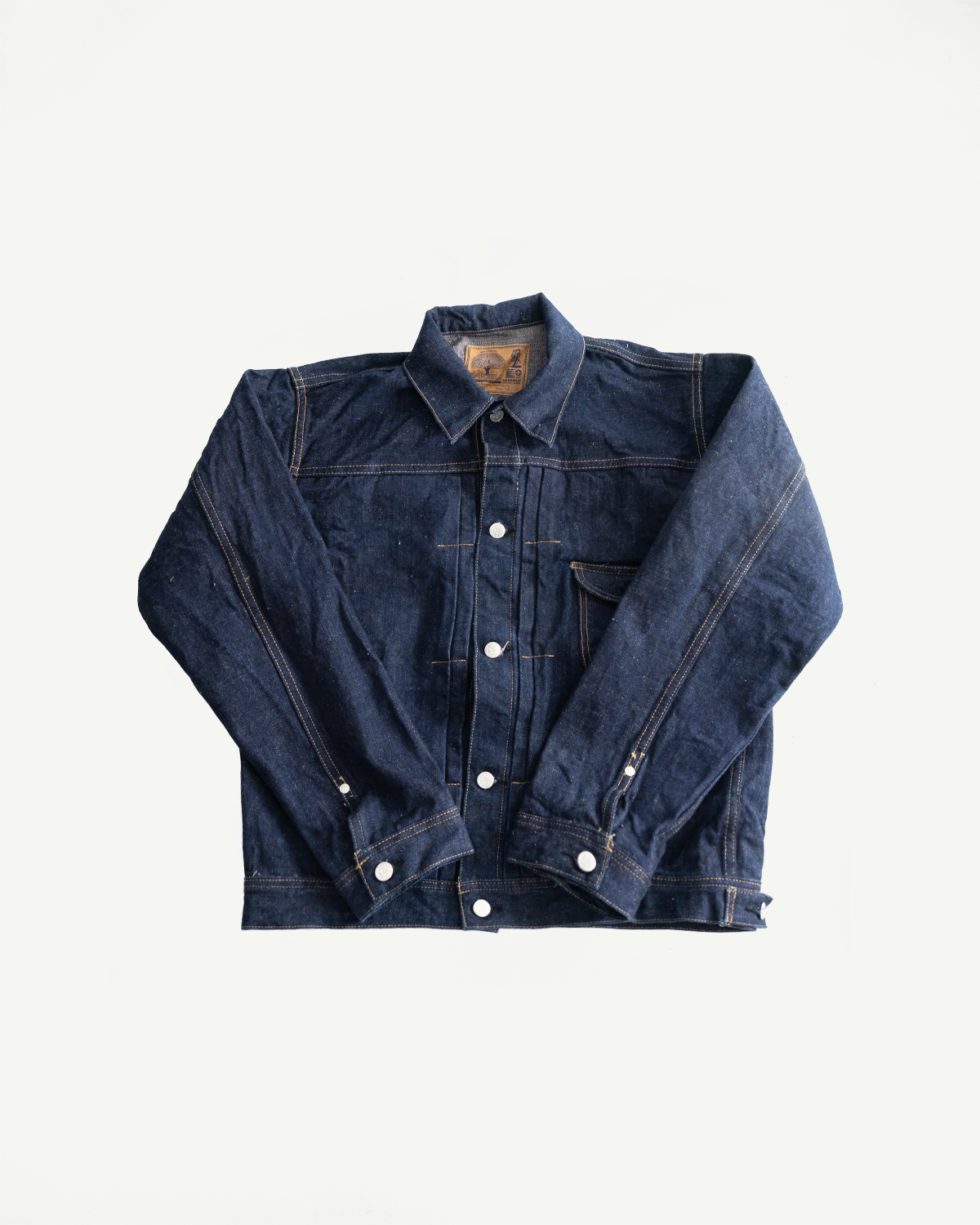 Flat lay of front side of indigo denim jean jacket, showing collar, button details, and chest pocket.
