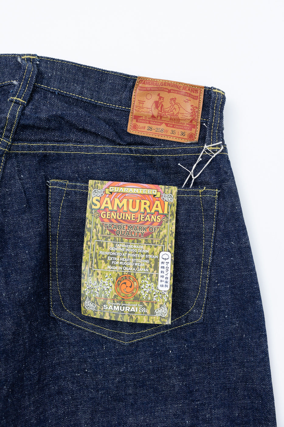 Close-up of Samurai Jeans back waist patch and rear pocket label, showcasing denim texture and stitching, rear view.