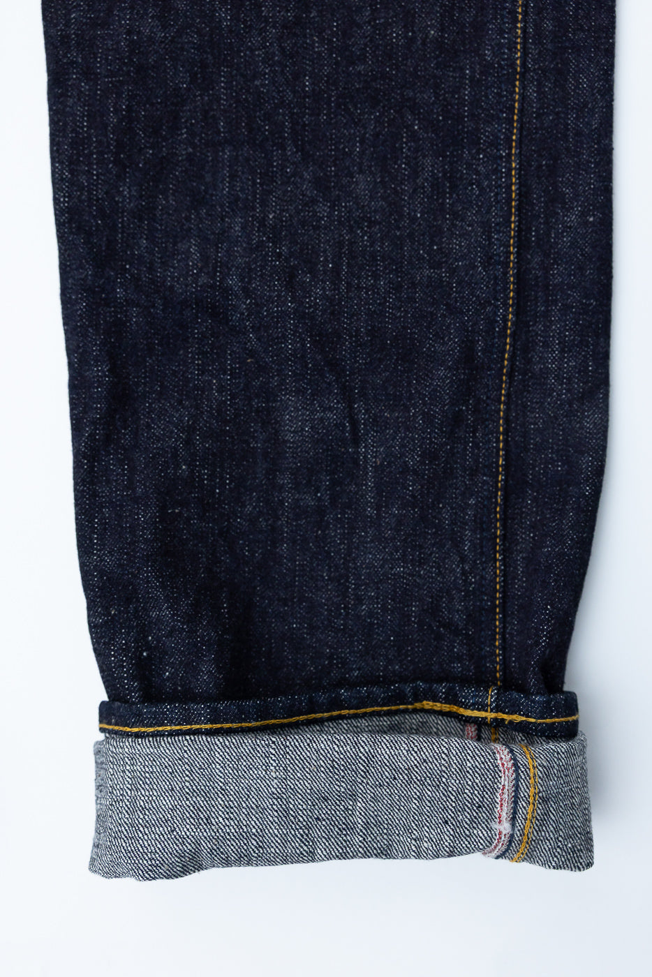 Close-up of raw selvedge denim jeans leg, front view, showing cuffed hem, yellow stitching, and fabric texture