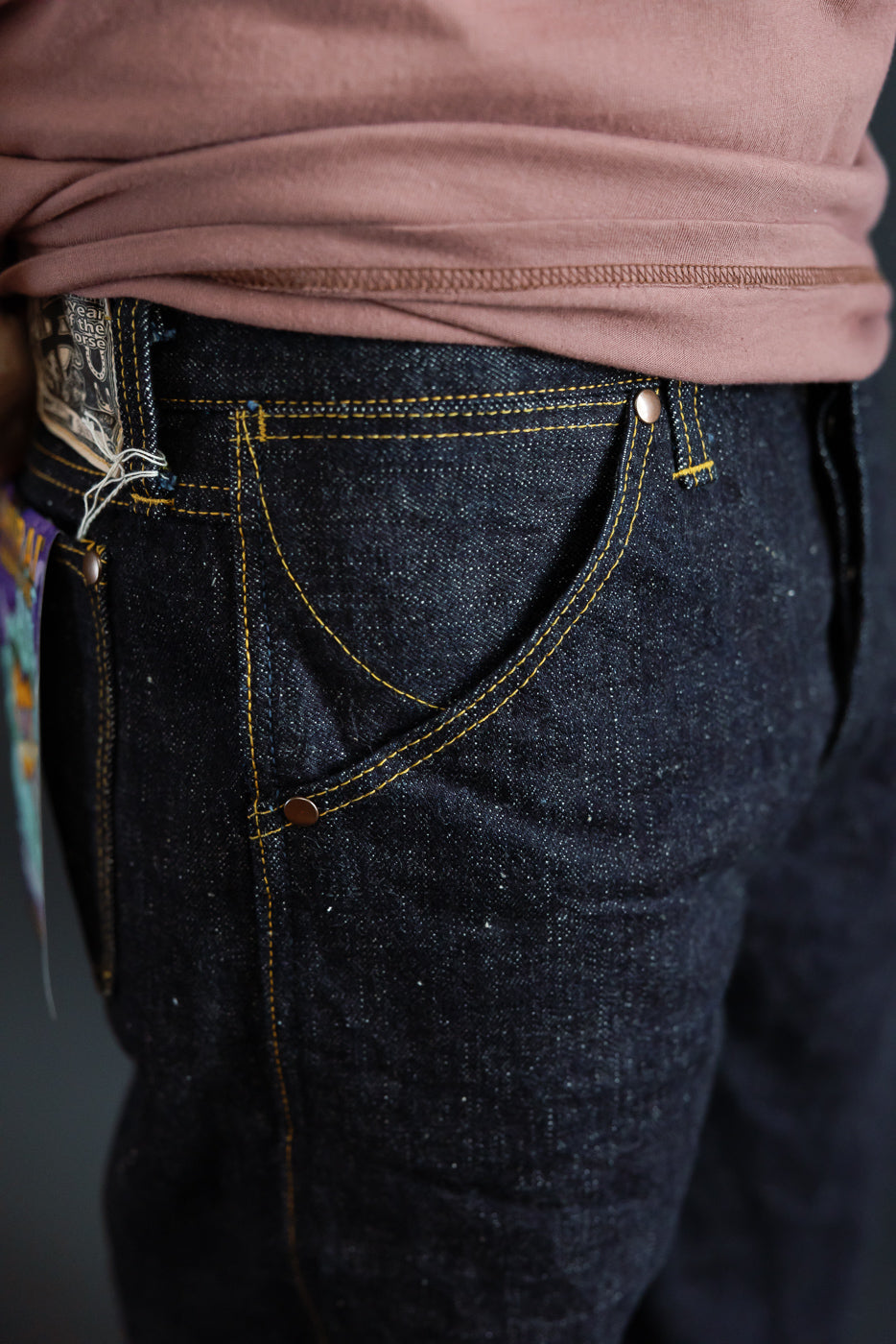 Close-up front view of dark selvedge jeans with yellow stitching, worn by male model, 5'9