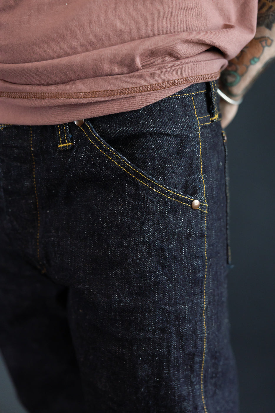 Close-up front view of dark selvedge jeans with yellow stitching, worn by male model, 5'9