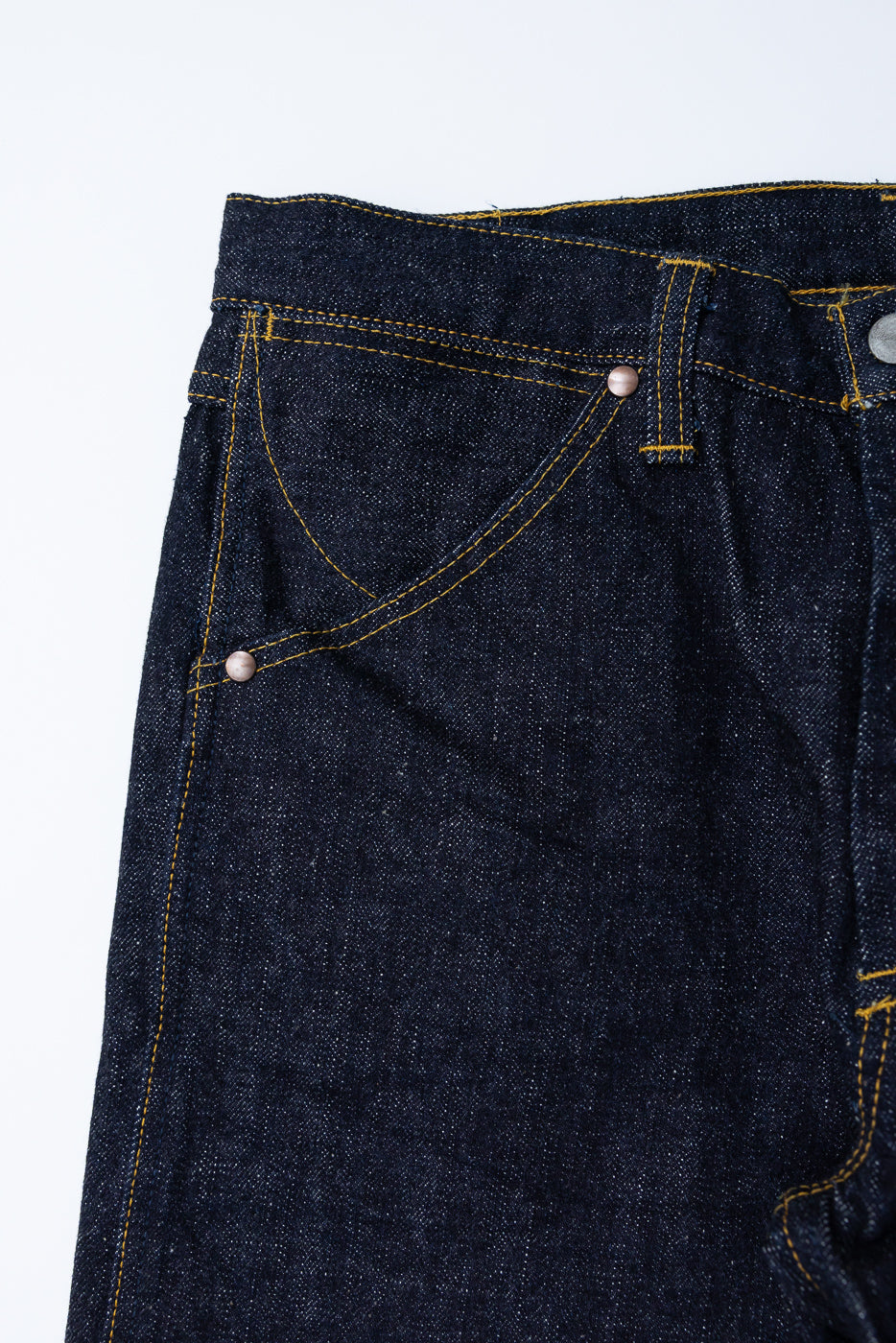 Close-up front view of dark selvedge denim jeans with gold stitching, copper rivets, and raw hem detail