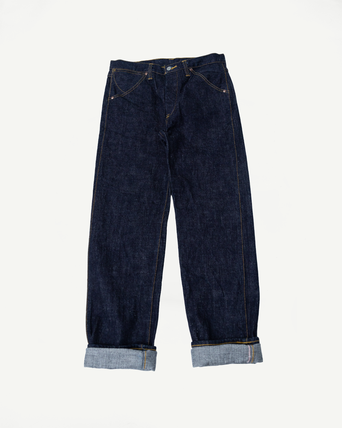 Front flat lay of dark selvedge denim jeans with rolled cuffs, showcasing stitching and fabric texture.