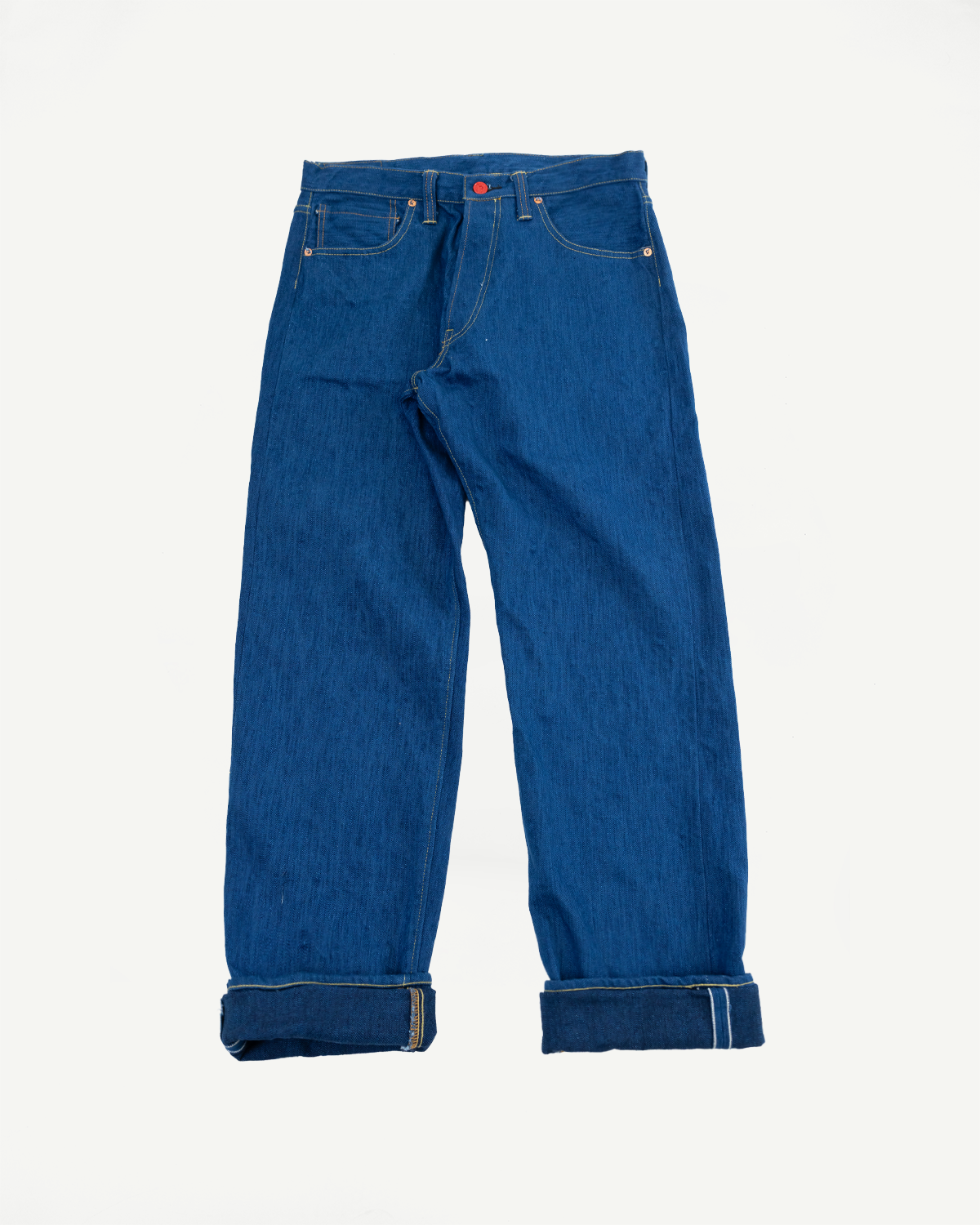 Front view flat lay of raw selvedge denim jeans with cuffed hems, red button, and contrast stitching