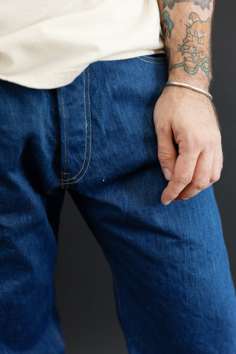 Close-up front view of men's selvedge denim jeans, showcasing yellow stitching and fabric texture on athletic build model