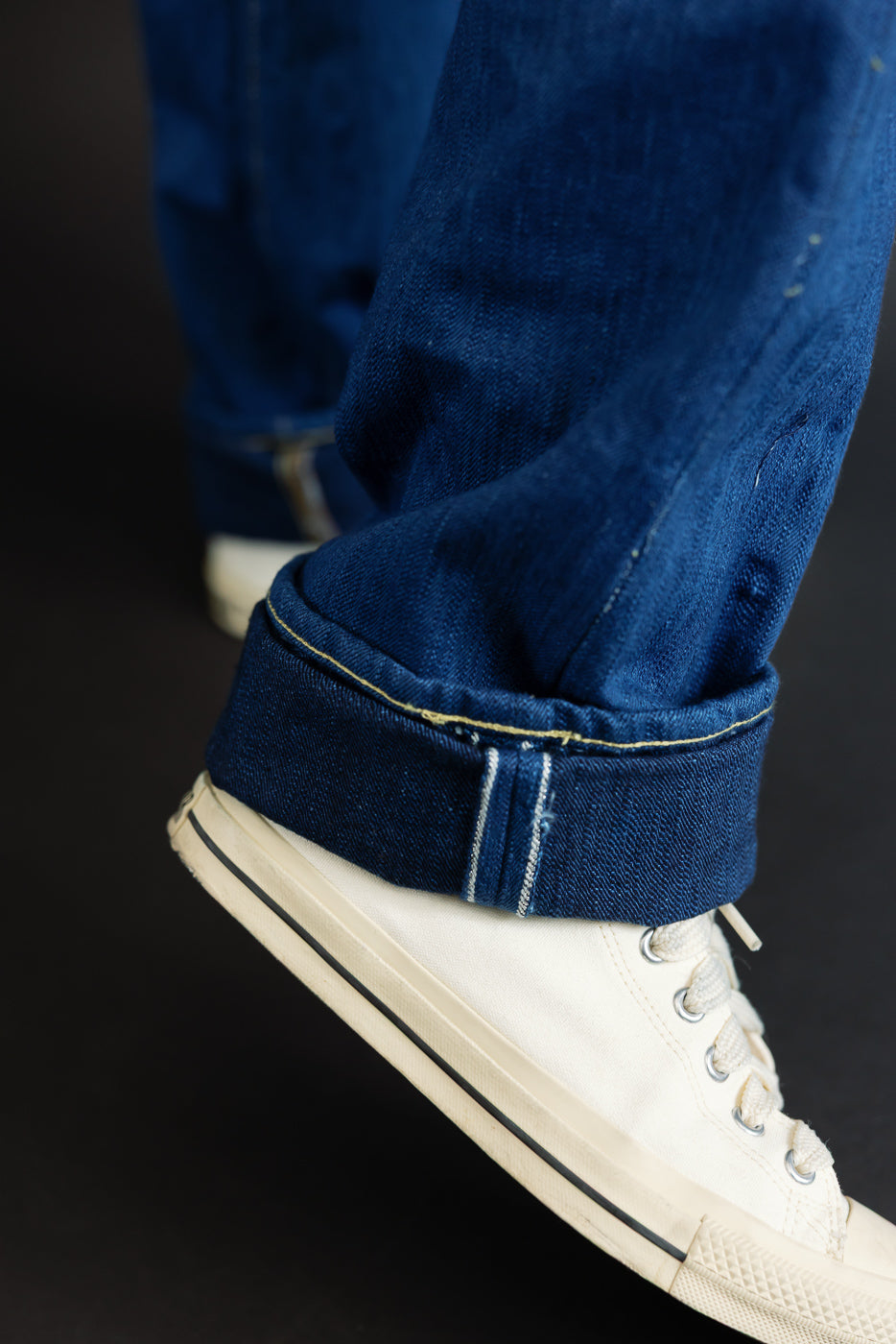 Close-up of male model’s cuffed selvedge denim hem with contrast stitching, paired with white sneakers